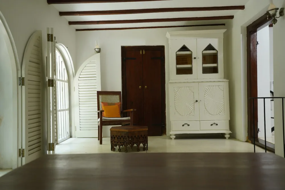 The black raja bedroom in Adigar's manor, featuring white walls and polished wooden floors in a bright, airy setting.