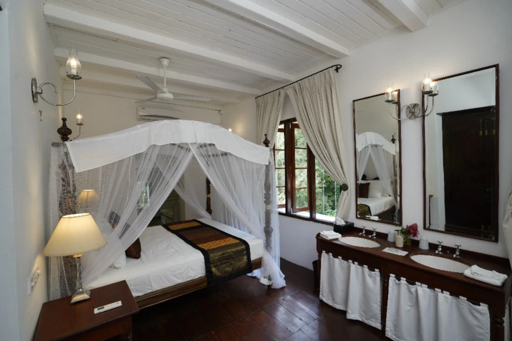 A luxurious bedroom featuring a canopy bed and dual sinks, located in the India Admiral bedroom of Adigar's Manor.