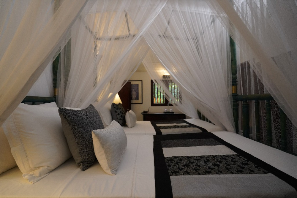 A canopy bed with white sheets and a canopy, set in the pioneer room of Adigar's manor