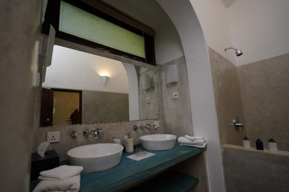 Interior of the pioneer room's bathroom in Adigar's Manor, showcasing two sinks and a mirror on the wall.