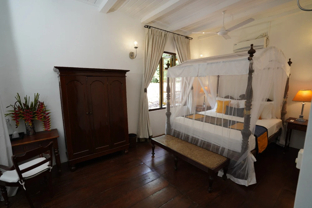 Sunbeam bedroom at Adigar's manor, showcasing a bed, a table, and a chair.