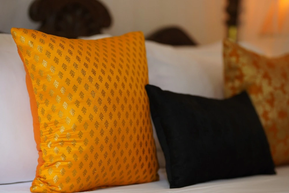 A cozy bed featuring orange and black pillows, illuminated by sunlight in Sunbeam room in Adigar's manor.