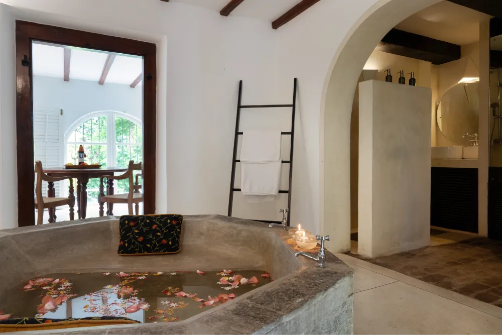 Elegant stone bathtub adorned with floating petals in the Black Raja Suite bathroom at Adigar’s Manor, blending Kandyan heritage charm with refined luxury