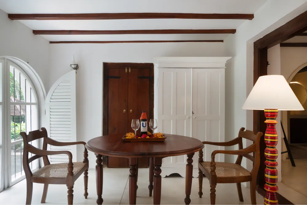 Stylish Black Raja Room lounge area with wooden dining table, colonial-style chairs, arched windows, and warm contemporary décor
