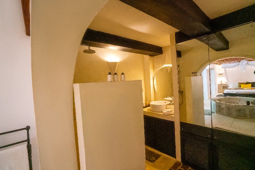 Warmly lit heritage bathroom in the Black Raja Suite at Adigar’s Manor featuring elegant archways, rustic beams, and a luxurious stone soaking tub