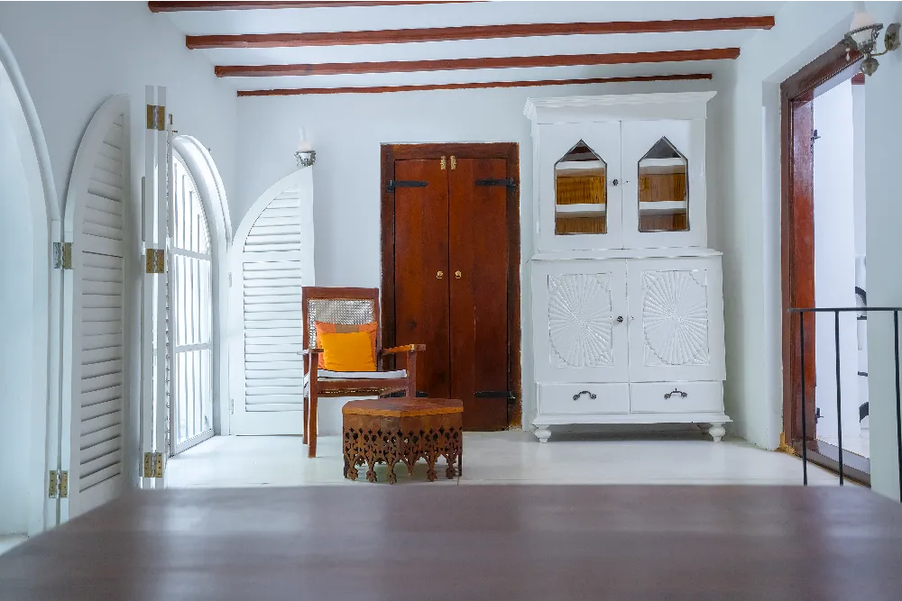 Bright Black Raja Room interior with arched shutter windows, handcrafted white cabinet, wooden accents, and elegant colonial-style décor