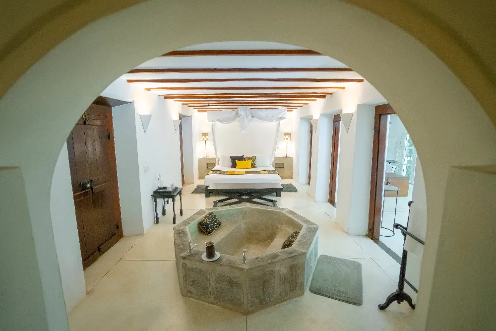 Luxurious Black Raja Room featuring a spacious open-plan layout with a canopy bed, central stone bathtub, and elegant colonial-inspired interiors