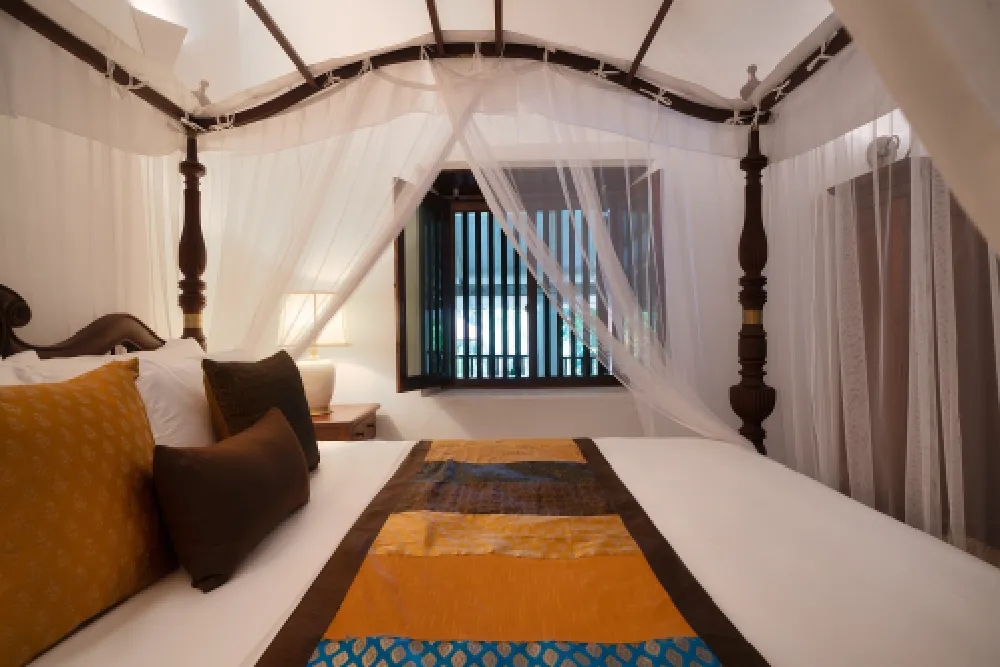 Cornelian Room featuring a luxurious four-poster canopy bed, flowing sheer drapes, warm ambient lighting, and elegant colonial-style décor