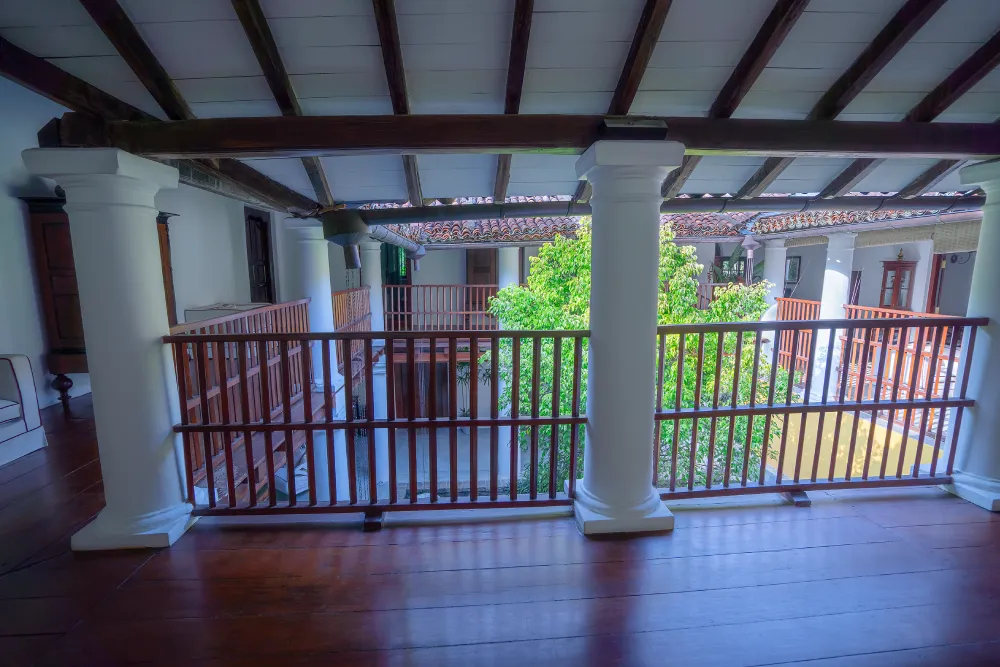 Open-air colonial-style upper veranda with wooden railings, white pillars, and courtyard garden view in a luxury heritage villa