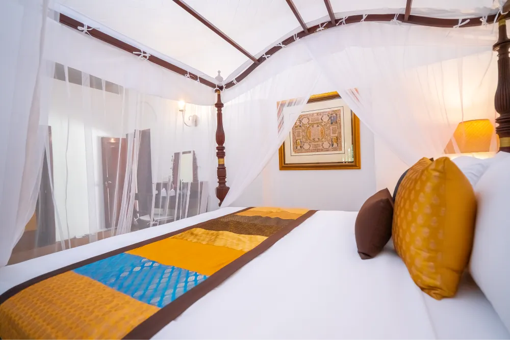 Cornelian Room with elegant four-poster canopy bed, sheer white drapes, vibrant golden cushions, and warm boutique-style interior décor
