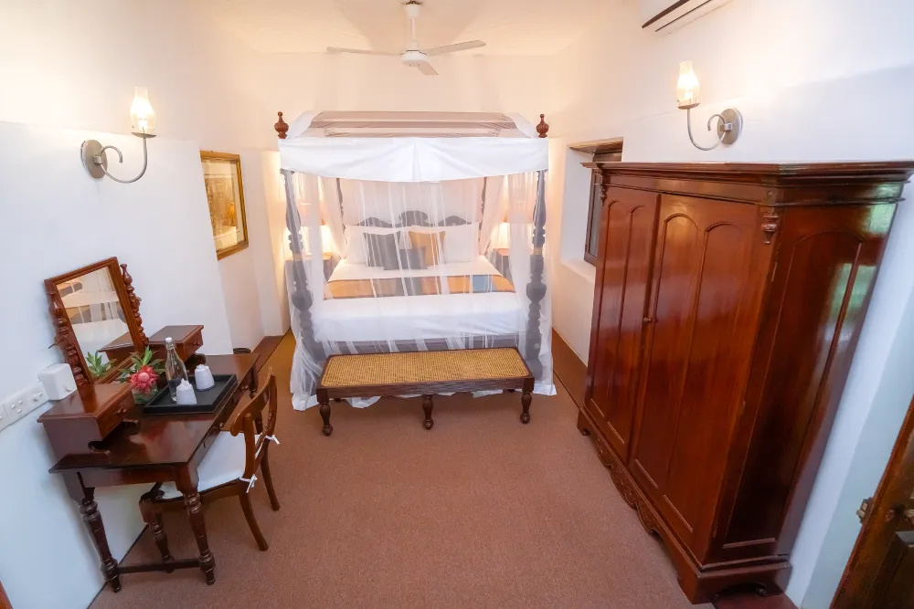 Cornelian Room with elegant four-poster canopy bed, antique wooden wardrobe, classic writing desk, and warm colonial-style interiors”