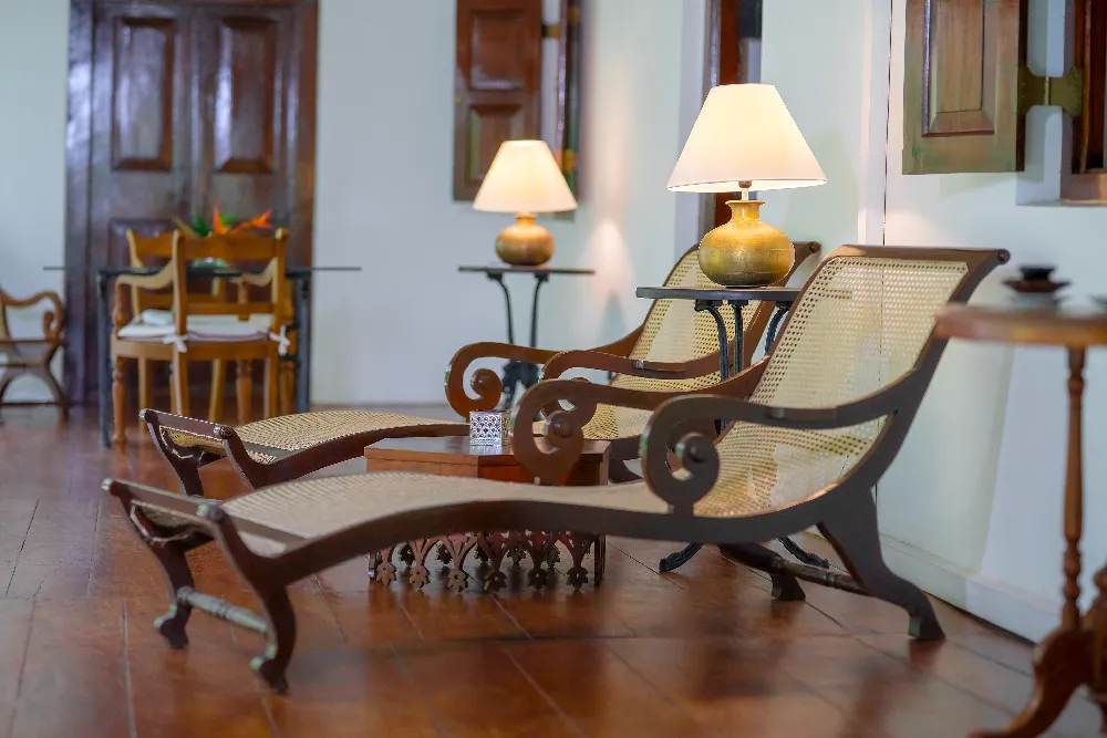 Elegant indoor lounge area with colonial-style wooden chaise lounges, warm table lamps, and sophisticated heritage-inspired décor