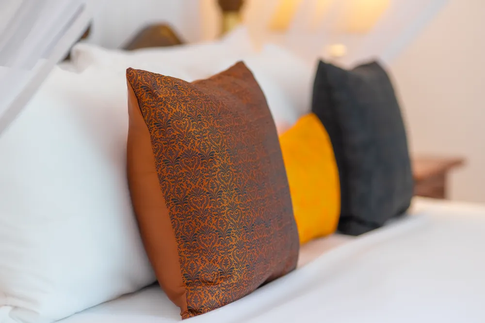 Close-up of decorative pillows on the Indian Admiral Room canopy bed, featuring rich earthy tones and elegant patterned fabrics