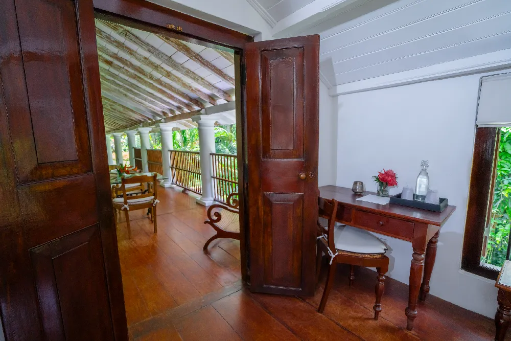 Indian Admiral Room interior with polished wooden floors, antique writing desk, and open doorway leading to a spacious colonial-style balcony
