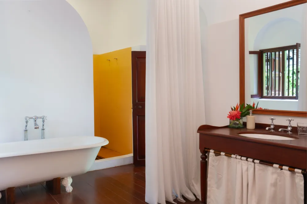 Lime Butterfly Room bathroom with freestanding bathtub, elegant wooden vanity, soft white drapes, and bright tropical luxury interiors