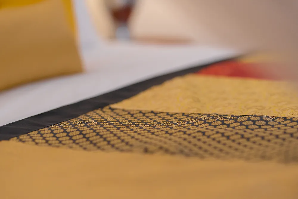 Close-up detail of elegant golden patterned bed runner in the Lime Butterfly Room with warm luxury bedroom ambiance