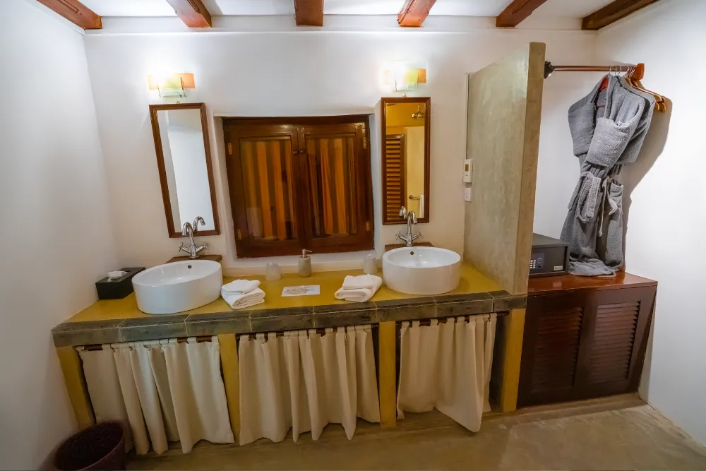 Monkey Puzzle Room bathroom with twin vessel sinks, soft lighting, luxury bathrobes, and warm colonial-style finishes