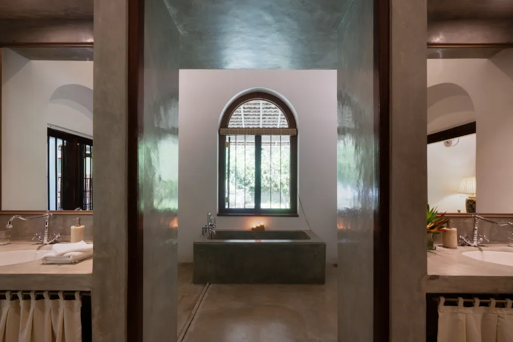 Peacock Royal Room bathroom featuring a luxurious stone soaking tub, twin vanity spaces, elegant arched window, and refined tropical colonial interiors