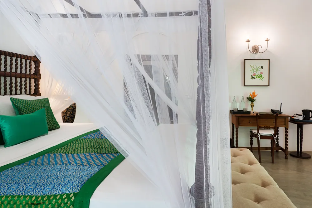 Peacock Royal Room with elegant four-poster canopy bed, flowing white curtains, handcrafted wooden furniture, and refined tropical luxury décor