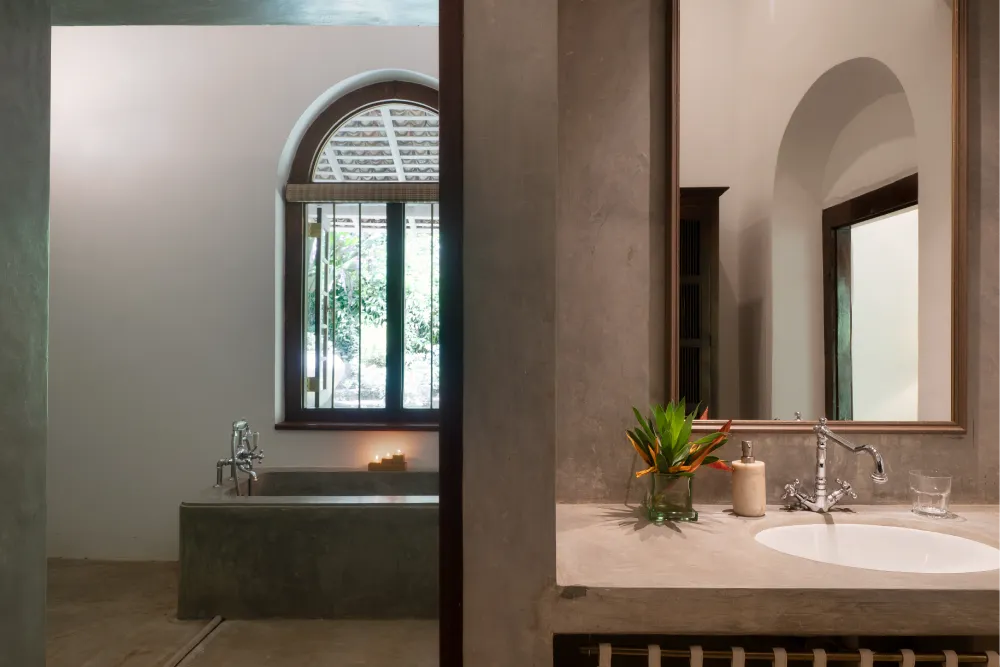 Peacock Royal Room bathroom with elegant stone bathtub, minimalist vanity, arched window, and serene tropical-inspired colonial design