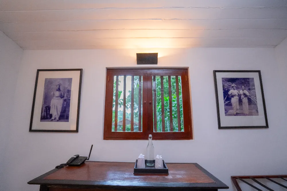 Writing desk and window area inside the Pioneer Room with framed vintage artwork, wooden furnishings, and garden view