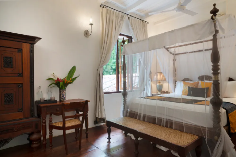 Sunbeam Room with elegant four-poster canopy bed, wooden furnishings, warm lighting, and serene garden-view window