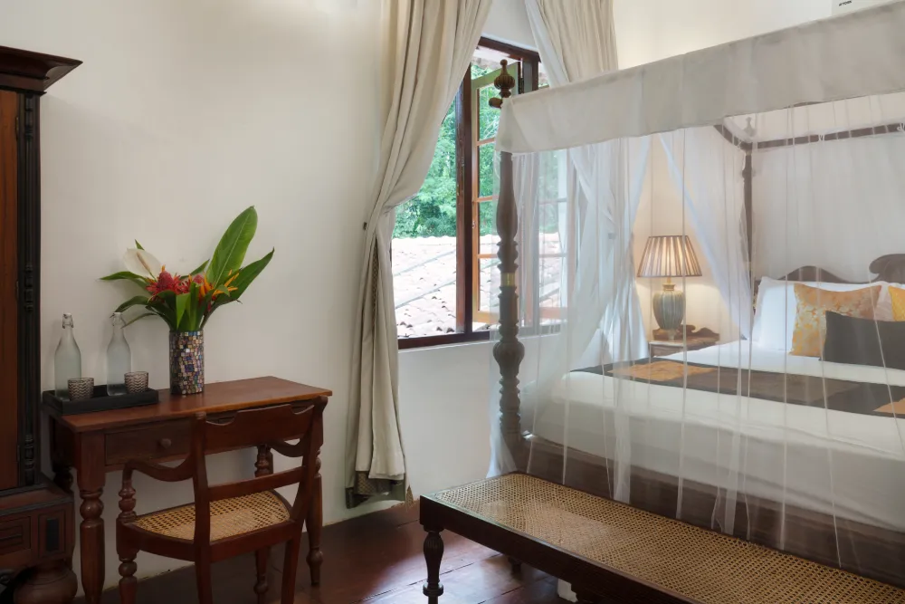 Sunbeam Room with elegant canopy bed, soft neutral décor, warm bedside lighting, and a window overlooking lush greenery