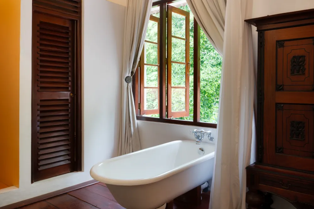 Elegant Sunbeam Room bathroom with a freestanding bathtub beside large open windows overlooking lush tropical greenery