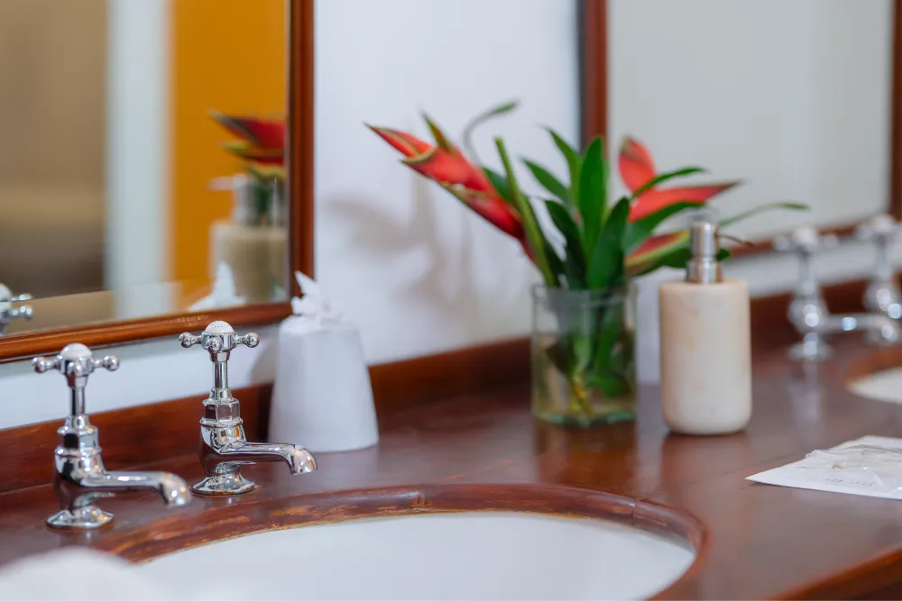 Close-up of the Sunbeam Room bathroom vanity featuring polished chrome taps, wooden countertop, tropical flowers, and elegant bathroom amenities