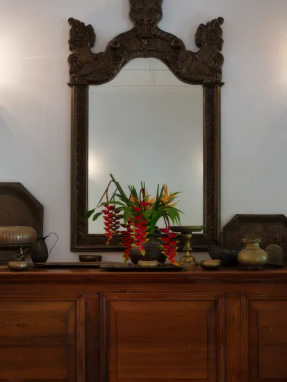 Traditional Kandyan-inspired wooden console with an ornate carved mirror and elegant floral arrangement at Adigar’s Manor