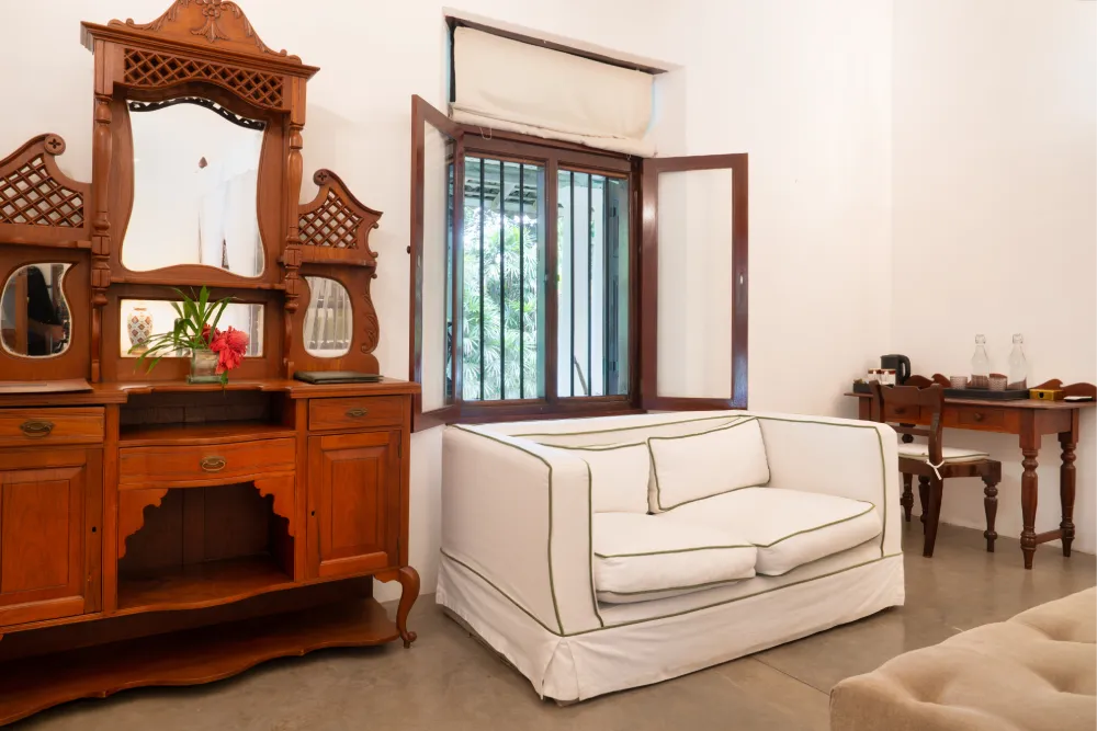 Redspot Duke Room featuring antique wooden dressing table, cozy lounge seating, open colonial-style window, and elegant tropical-inspired interiors